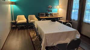 Una habitación con cama, dos sillas, escritorio con computadora, lámpara y ventana con cortinas.