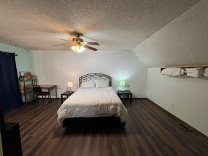 Ein Schlafzimmer mit Bett, Deckenventilator, zwei Nachttischen, Schreibtisch und Stuhl.