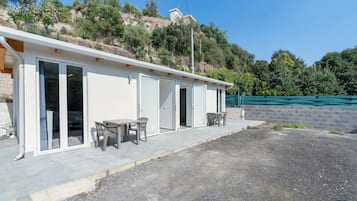 A modern building with a flat roof, large sliding glass doors, and a patio area with outdoor furniture.