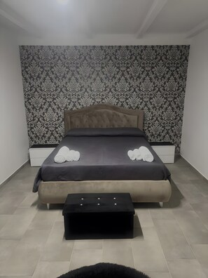 A bedroom with a tufted headboard, a bed with rolled towels, bedside tables, and a black ottoman.