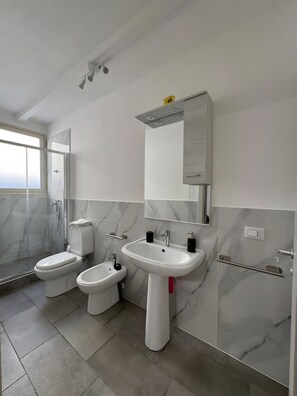 A modern bathroom with a toilet, bidet, and sink, marble walls, and a large mirror.