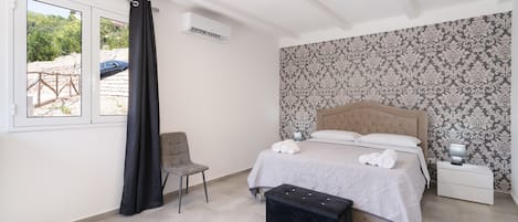 A bedroom with a bed, a chair, a bedside table, a lamp, and a window with curtains.