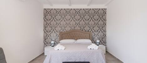 A bedroom with a bed, two bedside tables, a lamp, a chair, and a black ottoman.