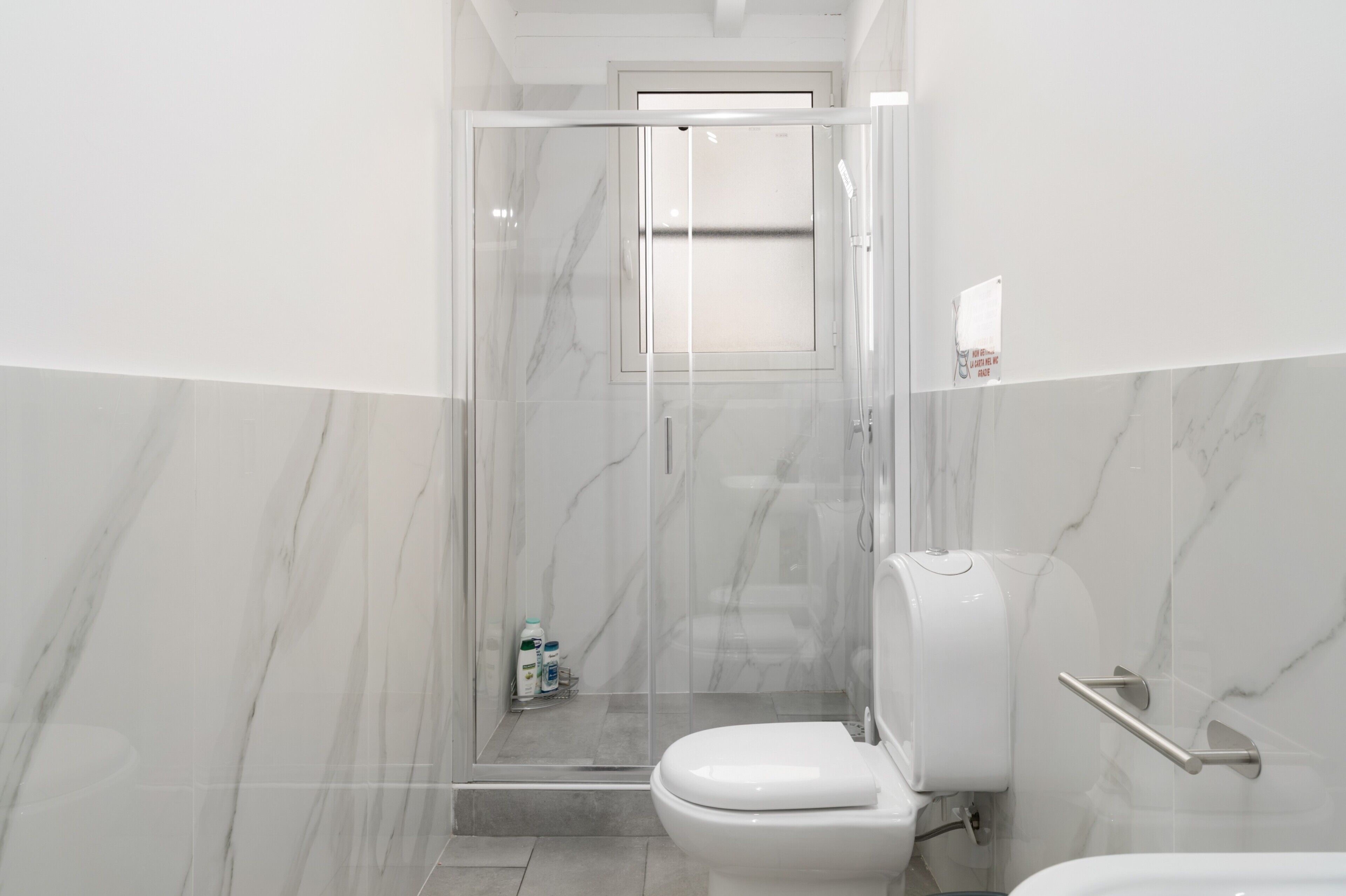 A modern bathroom with a glass-enclosed shower, a toilet, and a hand dryer.