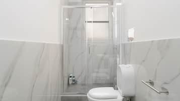 A modern bathroom with a glass-enclosed shower, a toilet, and a hand dryer.