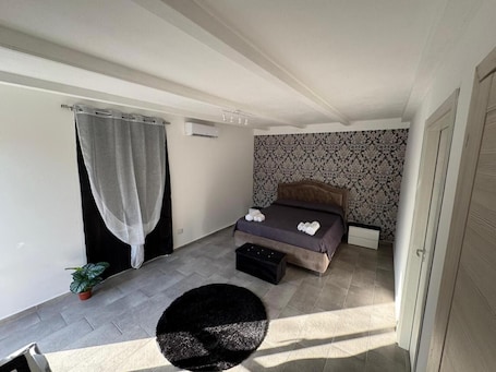 Una camera da letto con un letto, un comodino, una pianta in vaso e un tappeto rotondo nero.. Appartamento 'Oasi San Paolo' con piscina condivisa, Wi-Fi e aria condizionata