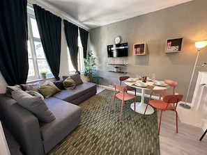 Un salon moderne avec un canapé, une table à manger, des chaises, un téléviseur et une horloge au mur.