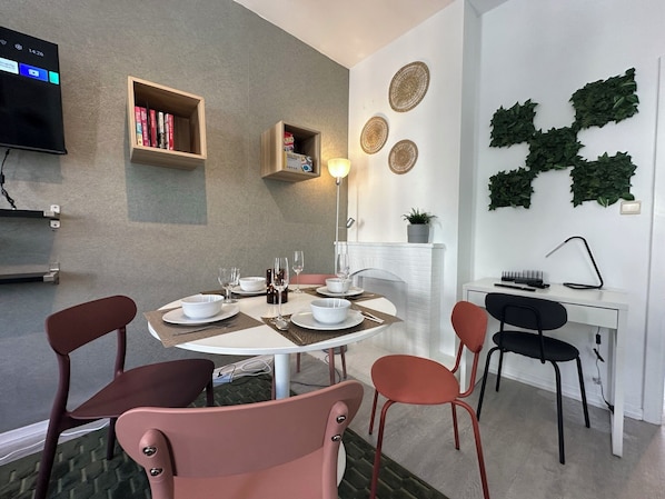 Un espace repas moderne avec une table ronde pour quatre personnes, entourée de chaises. Les murs sont ornés d’étagères et de tableaux décoratifs.