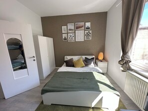 Et soveværelse med seng, garderobeskab, natbord med lampe og et vindue med gardiner.