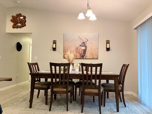 Ein Esszimmer mit Holztisch, sechs Stühlen, einer Kandelaber, Wandleuchten, einem Hirschgemälde und einem Wanddekor.