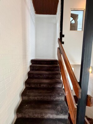 A staircase with a wooden handrail, white brick walls, and a dark carpeted floor.