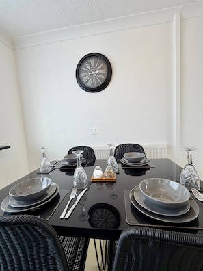 Una mesa de comedor dispuesta con platos, cubiertos y copas de vino, con un reloj montado en la pared.