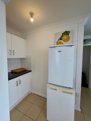 Una cocina compacta con armarios blancos, un refrigerador de dos puertas y una pequeña encimera.
