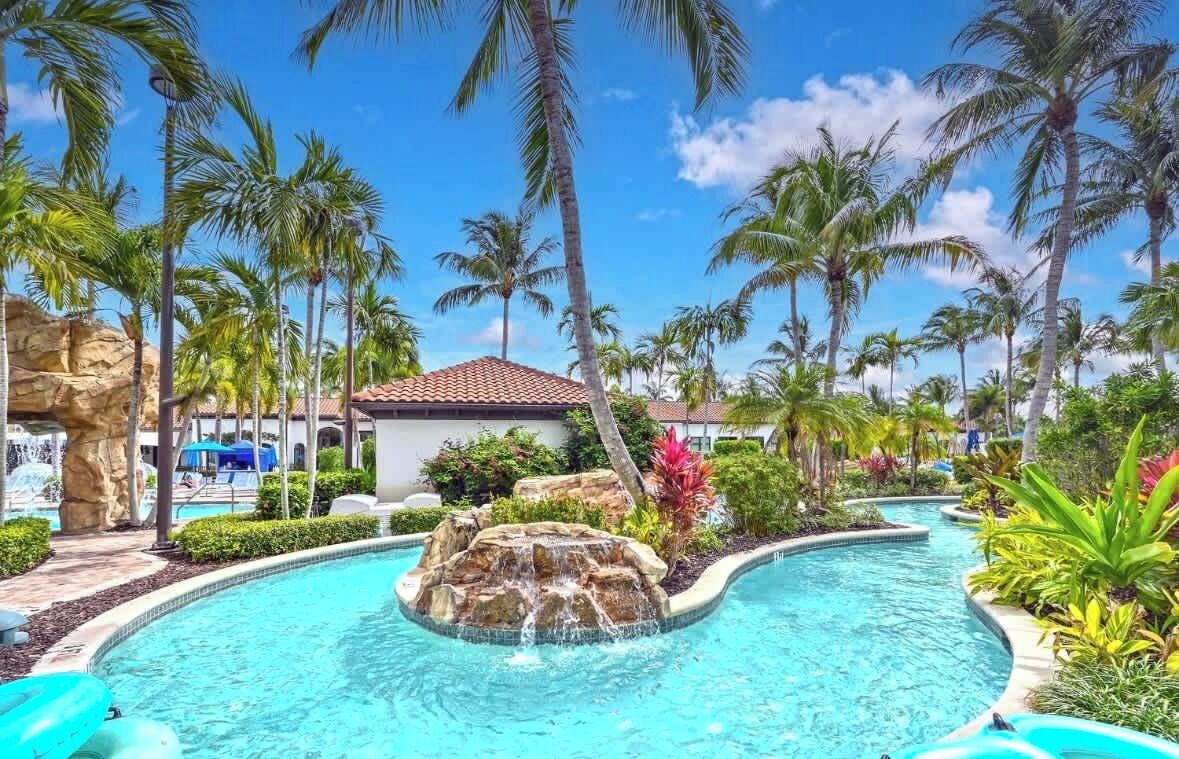 A resort pool with palm trees, a rock formation, and a small building.
