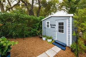 A small shed labeled 'Karaoke Room' with a wooden deck, potted plants, and a garden area. - 12 Min to Beach - Karaoke Room, Pool & Games (North Miami Beach)