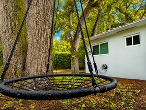 A hammock swing between trees, a white building with a window, and a blue hose on the wall. - 12 Min to Beach - Karaoke Room, Pool & Games (North Miami Beach)