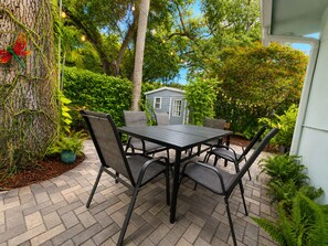 An outdoor patio with a table and chairs, surrounded by greenery and a small shed. - 12 Min to Beach - Karaoke Room, Pool & Games (North Miami Beach)