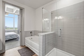 Ein modernes Badezimmer mit Duschkabine aus Glas, einer Badewanne und einem sichtbaren Schlafzimmer mit Bett und Ausblick.