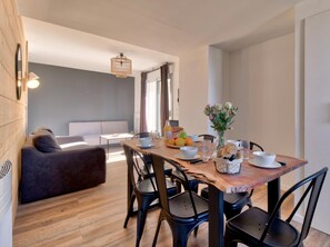 Ein moderner Essbereich mit einem Holztisch, schwarzen Stühlen und einer Couch im Hintergrund.
