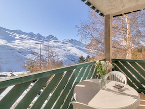 A balcony with a view of snow-covered mountains, a table with a vase of flowers, and a chair. - Résidence Les Balcons du Soleil 3P6S (Germ)