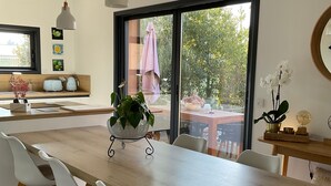 Una cocina moderna con una isla grande, sillas blancas, lámparas colgantes y vistas amplias por una ventana.