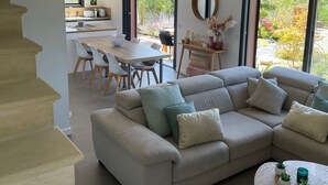 Una sala de estar moderna con un sofá seccional, un comedor con mesa y sillas, una escalera y ventanas amplias con vistas al exterior.