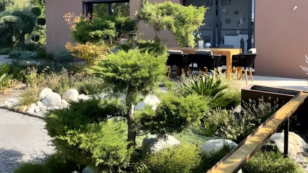 Un edificio moderno de dos pisos con un jardín ajardinado que presenta una variedad de plantas y una terraza de madera.