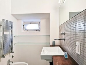 A bathroom with a white sink, a glass shelf, a towel rack, and a window. - Vrbo Property (Bari)