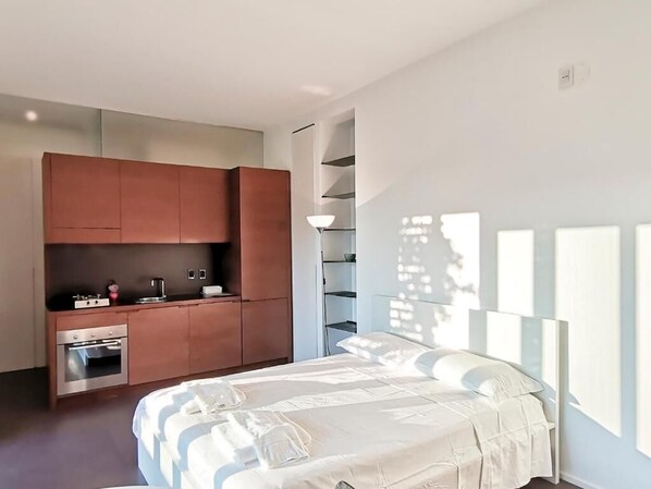A modern bedroom with a bed, a built-in kitchen area, and a staircase. - Vrbo Property (Bari)