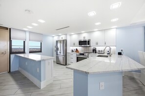 A modern kitchen with white cabinets, stainless steel appliances, and a large island with a marble countertop.