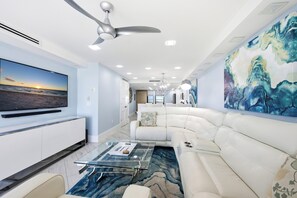 A modern living room with a flat-screen TV, a ceiling fan, and a large abstract painting.