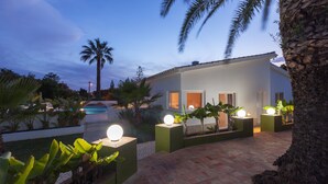 Et moderne hus med pool, omgivet af tropiske planter og palmer.