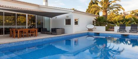 Une maison moderne dotée d’une piscine, de mobilier d’extérieur et d’un patio couvert.