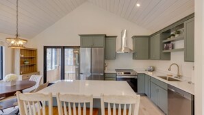 Une cuisine moderne dotée d’un grand îlot central, d’appareils électroménagers en acier inoxydable et de meubles de couleur vert clair.