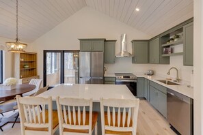 A modern kitchen with a large island, stainless steel appliances, and light green cabinetry. - Modern Mountain Retreat at Waterville Estates (Campton)