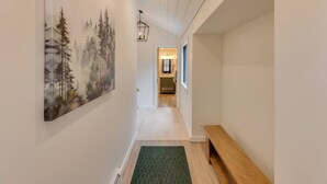 Un couloir orné d’un tableau représentant des arbres, avec un banc en bois et un luminaire.
