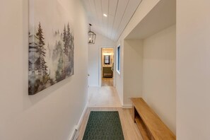 A hallway with a painting of trees, a wooden bench, and a light fixture. - Modern Mountain Retreat at Waterville Estates (Campton)