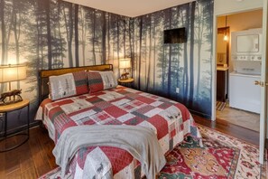 Een slaapkamer met een groot bed, een wand met een bosmotief, een televisie en een kitchenette.