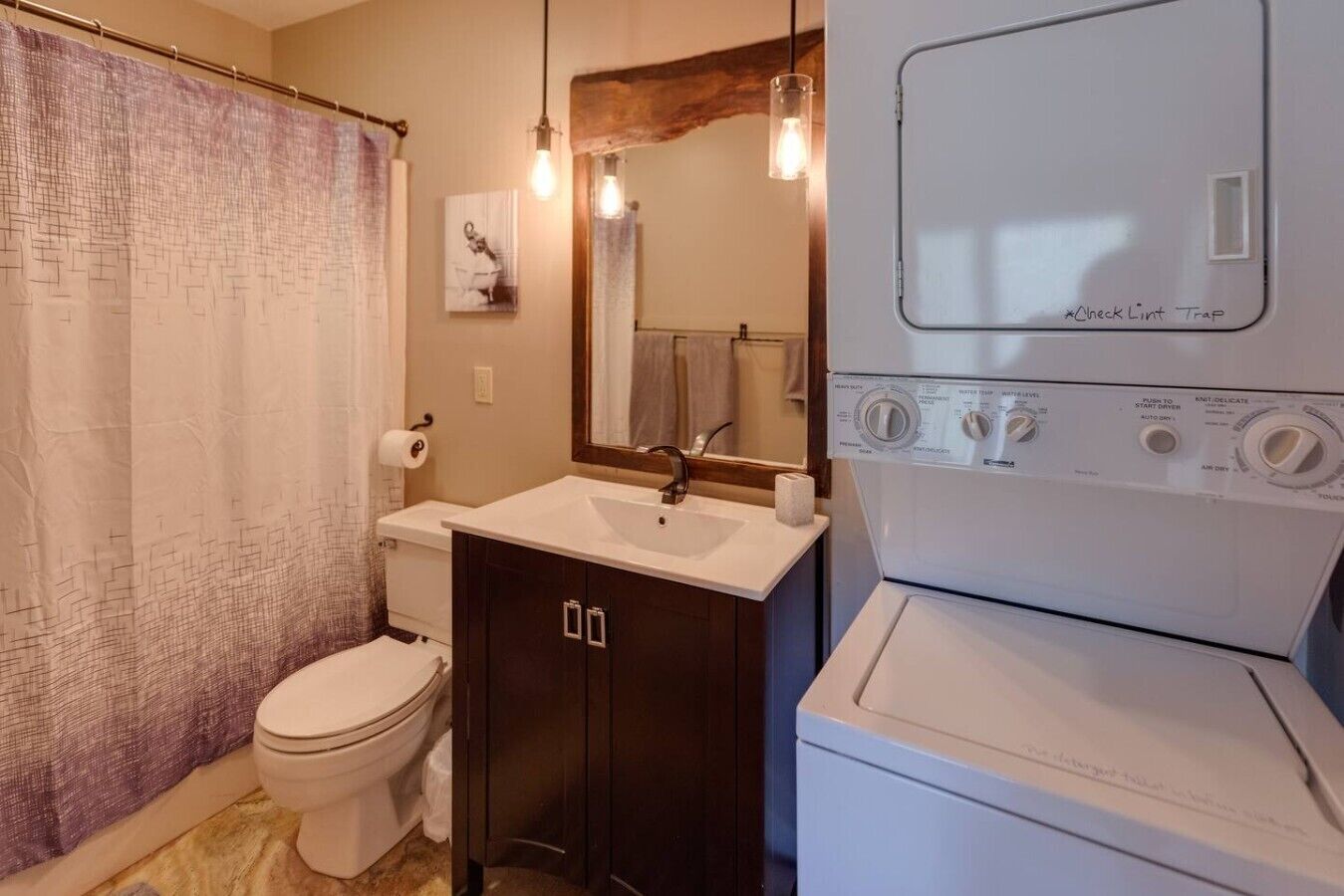 Une salle de bain équipée de toilettes, d’un lavabo, d’un miroir, ainsi que d’un lave-linge et d’un sèche-linge superposés.