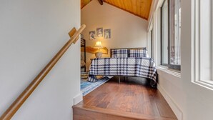 Eine Treppe führt zu einem Schlafzimmer mit einem karierten Bettbezug, einer Lampe und Wandbildern im maritimen Stil.