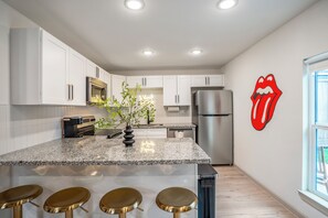 Une cuisine moderne avec des armoires blanches, des appareils en acier inoxydable, un comptoir en granit et le logo des Rolling Stones sur le mur.
