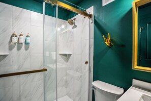 Un baño con cabina de ducha de vidrio, azulejos de mármol blanco, un inodoro y un lavabo.