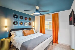 Une chambre à coucher avec un lit, un ventilateur de plafond, des platines vinyles fixées au mur et une fenêtre avec des rideaux.