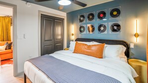 A bedroom with a bed, ceiling fan, wall-mounted record player lights, and a door leading to another room.