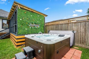 Un jacuzzi con revestimiento de madera, una terraza de madera y una pared verde con flores blancas.
