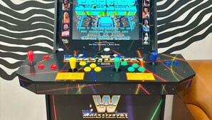 A wrestling arcade machine with a screen displaying a wrestling game, joystick controls, and a power outlet.
