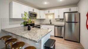 A modern kitchen with white cabinets, stainless steel appliances, a granite countertop, and a bar stool area.