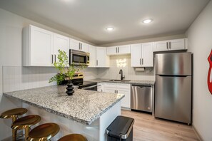 Una cocina moderna con armarios blancos, electrodomésticos de acero inoxidable, encimera de granito y una zona con taburetes de bar.