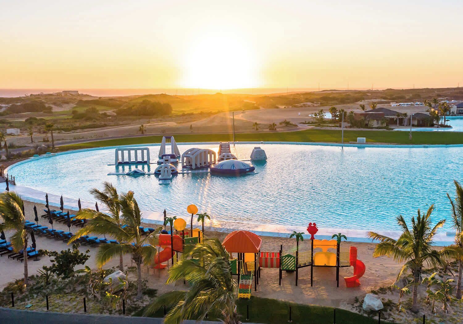 A large swimming pool with water slides, surrounded by palm trees and lounge chairs.