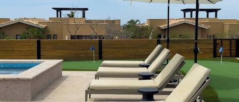 A poolside area with lounge chairs and an umbrella, a pool, and a wooden fence.